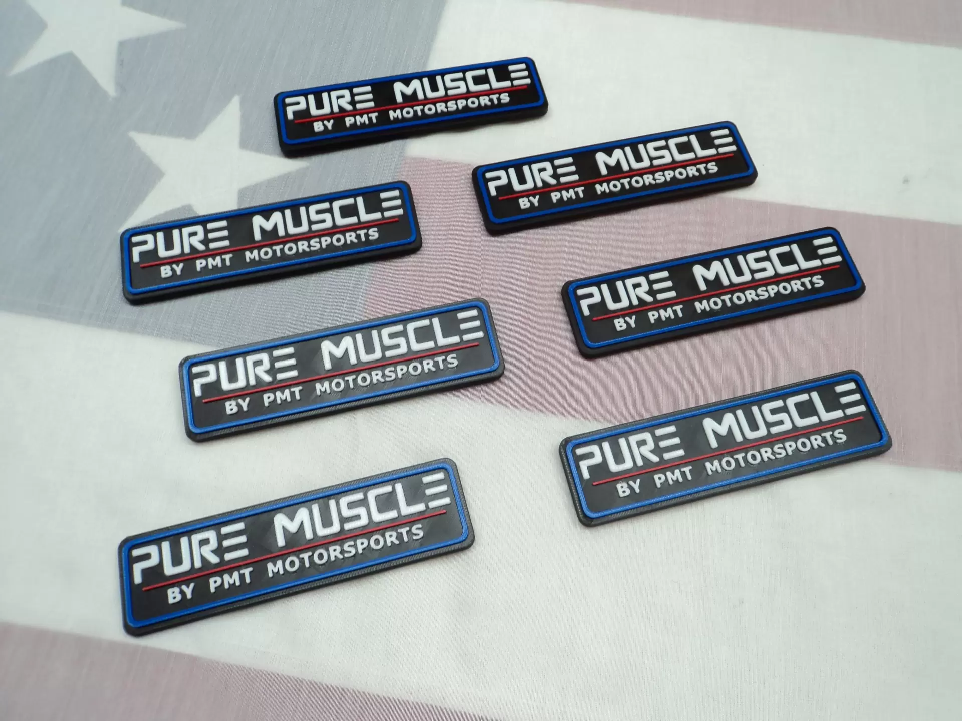 Several black patches with blue borders reading 'PURE MUSCLE BY PMT MOTORSPORTS' scattered on a stars-and-stripes background.
