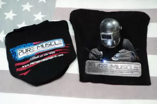 Two black shirts: left shows a blue-and-red Pure Muscle logo; right features a welding scene with a metallic badge reading 'Pure Muscle by PMT Motorsports'; background is a flag pattern.