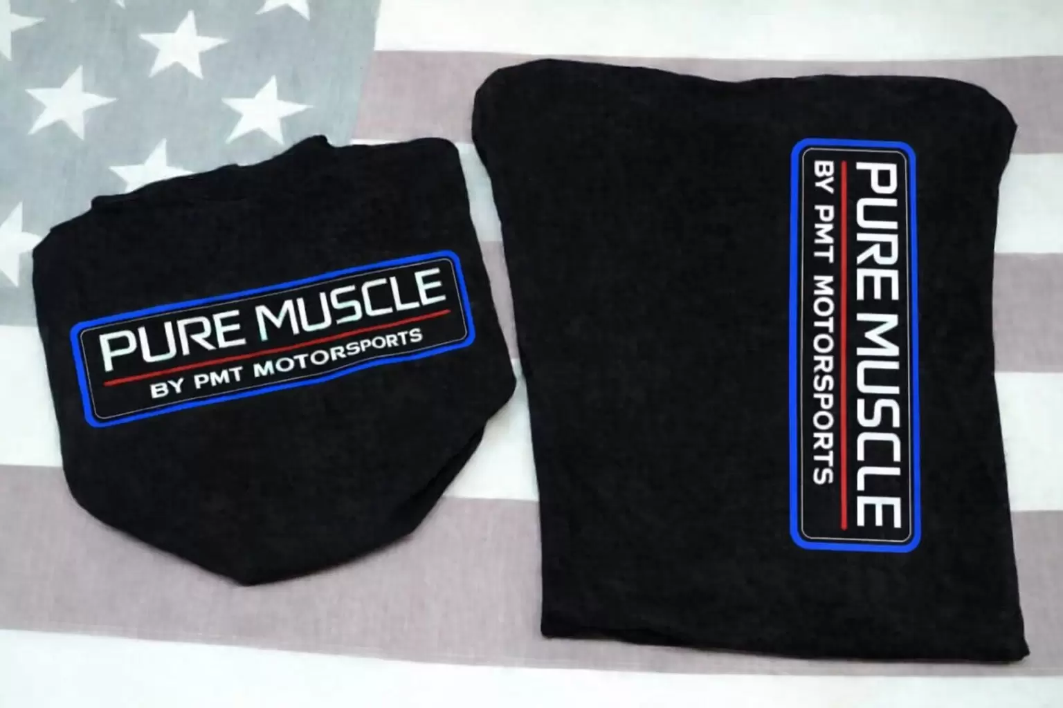 Two black clothing items, each with a blue-bordered logo reading 'PURE MUSCLE BY PMT MOTORSPORTS' set on a light American flag background.